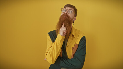 Wall Mural - Thoughtful bearded redhead man wearing glasses and a colorful shirt, isolated over yellow background.