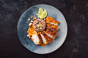 Roasted spicy butter chicken breast fillet in red curry gravy sauce with red rice, coconut and cashew nuts served as top view on a design plate with copy space