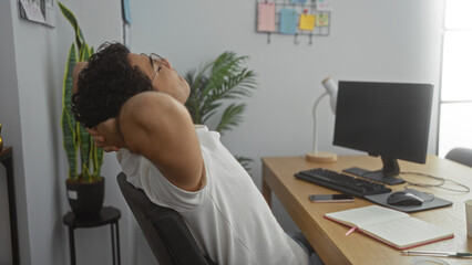 Sticker - Handsome young hispanic man in an office setting relaxing at his desk with a computer, notebook, and plant in the background.