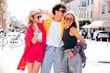 © halayalex - Group of young three stylish friends posing in the street. Fashion man and two cute female dressed in casual summer clothes. Smiling models having fun. Cheerful women and guy outdoors, sunglasses