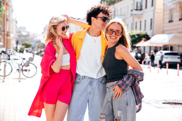 Wall Mural - Group of young three stylish friends posing in the street. Fashion man and two cute female dressed in casual summer clothes. Smiling models having fun. Cheerful women and guy outdoors, sunglasses