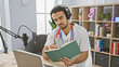 © Krakenimages.com - A handsome young man in headphones and a lab coat reads a book near a microphone in a podcast studio setting.
