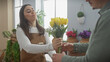 © Krakenimages.com - Woman florist handing yellow tulips to man in green flower shop filled with plants and natural light