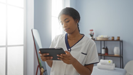 Young latina woman working on a tablet in an indoor spa setting with shelves in the background, showcasing a serene beauty and wellness environment.