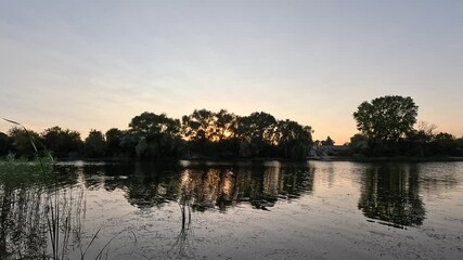 Wall Mural - sunset on the river. sunrise on the lake shore. sun behind the trees. beautiful natural landscape with sunset and water. high definition video. sun glare on water. dark water in the river.