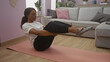 © Krakenimages.com - An african-american woman with curly hair is performing a yoga pose on a mat in a cozy living room, showcasing a relaxing indoor home atmosphere with soft lighting and modern decor.