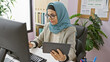 © Krakenimages.com - A mature woman in hijab using a tablet while working at her office desk dotted with plant and office supplies.