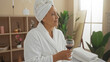© Krakenimages.com - Mature woman enjoying a relaxing drink in a serene spa room, dressed in a white bathrobe with a towel wrapped around her head.
