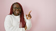 © Krakenimages.com - A smiling african american woman with braids wearing glasses and a white sweater poses against a pink background, pointing with her finger.