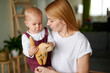 © khmelev - Blonde-haired mother and daughter. Mum holding one and a half year old daughter in her arms, the little girl is looking at an interesting toy.
