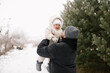 © VikaNorm - Bearded man is holding a smiling baby dressed warmly in a white overall and hat, surrounded by snow-covered ground and evergreen trees. Joyful moment between the father and little daughter in a winter