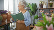 © Krakenimages.com - Senior woman wearing glasses and apron writing in notebook amidst vibrant flowers inside a cozy flower shop