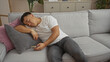 © Krakenimages.com - A young, handsome chinese man sleeps on a couch in his living room holding a smartphone, highlighting a relaxed indoor home environment.