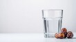 © Nataliia - Crystal-clear glass of water with a few dates on the side isolated on white background Basic iftar essentials emphasizing simplicity and purity