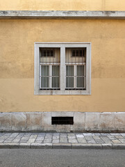 street view of old window with white stone frame against yellow rendered wall on building