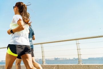 Two Joggers Running Along a Sunny Waterfront Path With a Clear Blue Sky on a Bright Day in an Urban Setting