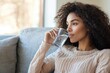© Vooglo - A serene image of a woman sitting on a couch, sipping a glass of water with a calm expression