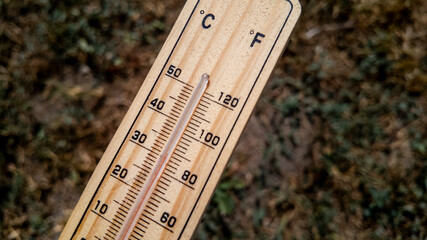 Close-up of a wooden thermometer on dry grass indicating extreme heat, relating to summer and climate change awareness