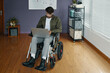 © DragonImages - Man with disability sitting in wheelchair and using laptop in office