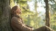 © B 7 YOU - A young man sits leaning against a tree in a forest with his eyes closed, enjoying the peace and quiet of nature.