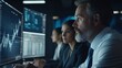 © Oulaphone - Professionals analyzing data on screens in a dimly lit office, focusing on financial charts and graphs.