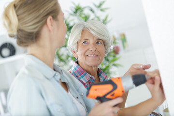 senior woman and daughter drilling a wall