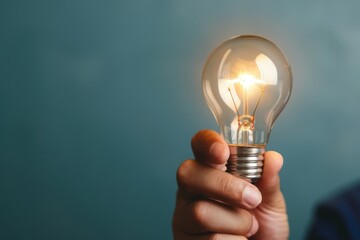 Hand holding a glowing light bulb, representing creativity, innovation, and bright ideas, set against a simple blue background.