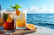 © Quality One   - Refreshing summer cocktails with ice and citrus garnishes are beautifully displayed against serene ocean backdrop, evoking sense of relaxation and enjoyment