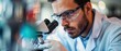 © Dalibor - Focused lab technician observing samples under microscope, wearing protective glasses and gloves.