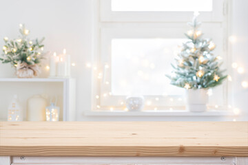 Wooden table top in front of blurred Christmas decorated window and shelf background