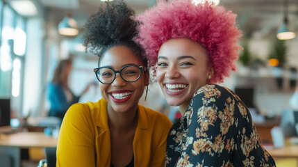 Two women with pink hair and glasses are smiling at the camera