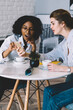 © BullRun - Surprised afro american female blogger feeling shocked from reading text message showed by caucasian friend sitting near, amazed women checking notification for smartphone gadget connected to 4g