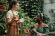 © AnnaStills - Smiling Caucasian waitress taking order in eco cafe, smiling female African American customer sitting at table and telling her order