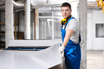 Professional engineer man in blue uniform works in factory. Rolled metal, metal processing and manufacturing of metal fence