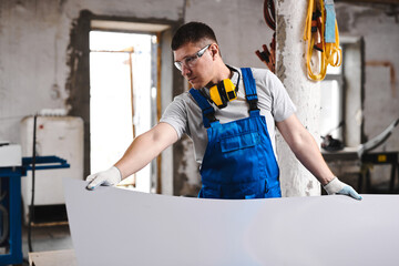 Professional engineer man in blue uniform works in factory. Rolled metal, metal processing and manufacturing of metal fence