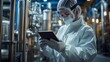 © Arieswanto - A worker in a sterile lab suit uses a tablet to monitor industrial equipment.
