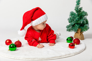 Wall Mural - Christmas portrait of cute little newborn baby girl, wearing red Santa hat with Christmas balls on a white background. Christmas and New Year concept