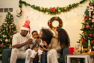 A lively Christmas celebration with three african friends enjoying drinks and holiday cheer on a sofa. The festive atmosphere includes Christmas trees, wreaths, lights, and decorations.