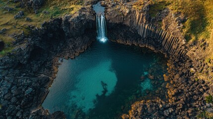 Sticker - Aerial view of a serene waterfall cascading into a clear, rocky pool surrounded by cliffs.