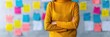 © Vilaysack - A person in a yellow sweater stands with arms crossed in front of a wall filled with colorful sticky notes in an office.