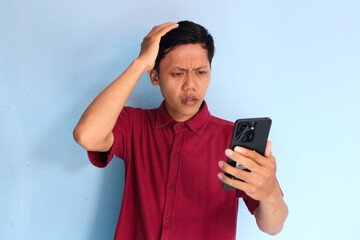 Young Asian man holding his mobile phone with sad expression