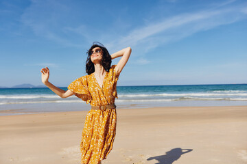 Poster - Woman in a yellow dress standing with arms outstretched on the sandy beach on a sunny day