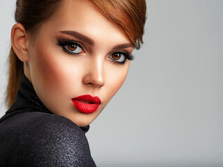 Beautiful girl with red lips and short hair. Pretty face of an young sensual woman. Closeup portrait of a model with bright makeup on a face. Attractive female posing at studio  in black closes.