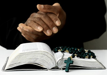 Wall Mural - black man praying to god with crucifix and hands together Caribbean man praying on black background with people stock photos stock image	