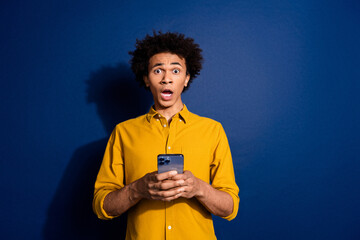 Wall Mural - Portrait of nice young man hold phone stare wear yellow shirt isolated on dark blue color background