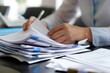 © miss irine - Female office employee works with documents at table. Close-up of hand holding pen, papers, file. Businesswoman organizes paperwork, checks financial data, signs contract. Office desk with many