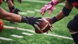 © miss irine - Close-up shot of American football ball between players hands on green field. Hands of athletes grasp football in game start. Kick off competition sport scene on grass field.