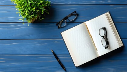 Minimalistic modern desk layout featuring glasses, a book, and a pen on a blue table with ample copy space in a top-down view