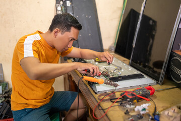 Asian male technician removing electronic circuitry while working at a service station