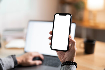 Wall Mural - hand holding texting using mobile on desk at home office, cell phone blank white screen mockup. back